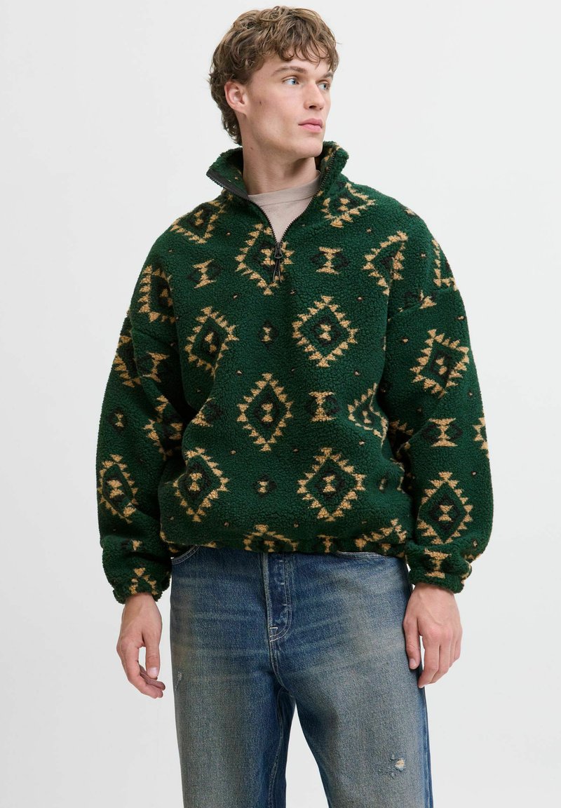 Zielony polarowy sweter z zamkiem przy kołnierzu, z geometrycznym brązowym i czarnym wzorem. Luźny krój z elastycznymi mankietami, miękka tekstura.