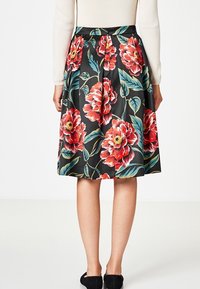 Jupe midi florale avec un fond noir, de grandes fleurs rouges avec des feuilles vertes, un design plissé et une taille avec fermeture éclair.