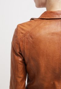 Giacca in pelle marrone, design aderente, dettagli di cucitura visibili, texture liscia e colletto a pescatore, mostrata di spalle.