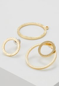 Ohrringe aus goldfarbenem Metall mit strukturiertem Finish. Enthalten sind drei kreisförmige Designs in unterschiedlichen Größen, wobei eines mit einem Steckerverschluss ausgestattet ist.