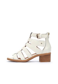 Sandalias de tacón de cuero blanco con múltiples correas verticales, un hebilla lateral y un tacón de madera; textura suave y detalles de costura.