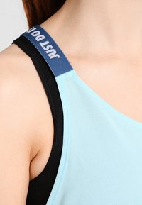 Jasnoniebieska i czarna bokserka z szerokim ramiączkiem; ramiączko ozdobione niebieskim materiałem z białym napisem "po prostu zrób to"; gładka faktura i dopasowany krój.