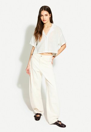 White cropped button-up shirt with short sleeves paired with wide-leg white pants and dark brown clogs featuring decorative hardware accents.
