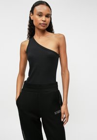 Μαύρο ριγέ bodysuit με έναν ώμο και εφαρμοστή γραμμή. Το μοντέλο συνδυάζει με μαύρα παντελόνια φόρμας που διαθέτουν κεντητό λογότυπο και ελαστική μέση.