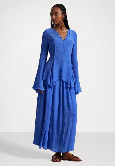 Dolga modra maksi obleka z teksturirano tkanino, z V-izrezom in gumbi na sprednji strani; ima razširjene rokave in plasteh rob.