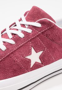 Red suede sneaker with white laces, featuring a white star logo and stitching. Rubber outsole with a black accent along the edge.