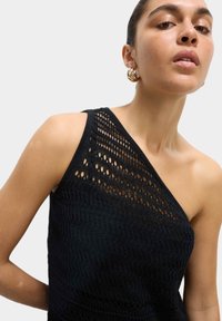 Haut tricot noir à une épaule avec un motif en zigzag texturé et un design à mailles ouvertes. Tissu léger avec une silhouette ajustée.