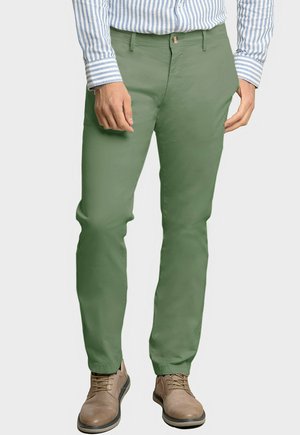 Chinos verdes de algodón con diseño de corte slim, que cuentan con una parte delantera plana, bolsillos laterales y cierre de botón. Combinados con zapatos marrones con cordones.