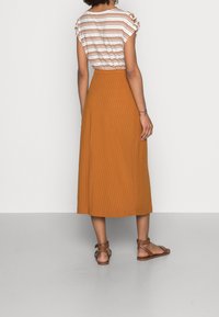 Falda midi de canalé marrón con cinturilla elástica. Combinada con una blusa blanca de rayas de manga corta y sandalias planas marrones.