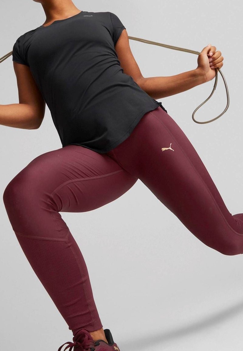 Svart figurnära t-shirt med korta ärmar, i kombination med vinröda leggings med ett texturerat mönster och en liten guldfärgad logotyp på låret.