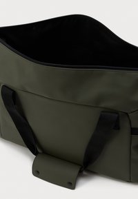 Ελαιόχρωμη, ανθεκτική στον καιρό τσάντα tote με μαύρο εσωτερικό, κλείσιμο με φερμουάρ και ανθεκτικές μαύρες λαβές; διαθέτει λεπτομέρεια με κλείσιμο τύπου snap.