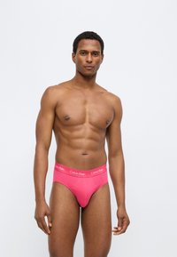 Ροζ βαμβακερά σλιπ με λευκή ελαστική μέση που φέρει το λογότυπο της Calvin Klein. Ομαλή υφή και εφαρμοστή σχεδίαση.