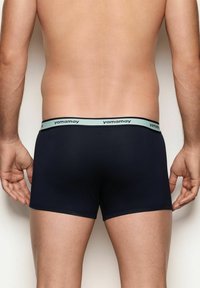 Uomo che indossa boxer in blu navy con un elastico verde chiaro con la scritta ripetuta "yamamay", mostrato da dietro.