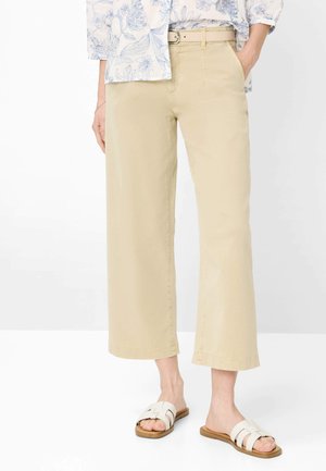 Beige, vidtbenede cropped bukser med bælte, båret med hvide slip-on sandaler og en blomsterprintet bluse med lange ærmer.