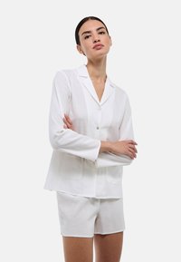 Chemise blanche en lin à manches courtes avec col revers et boutons à l'avant. Associée à un short blanc assorti, au design simple.