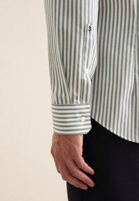 Camicia a righe in cotone verde e bianco, con polsini buttoned e un piccolo logo ricamato sulla manica, e un orlo curvo.