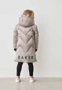 Piumino argentato con design a zigzag, dotato di un grande cappuccio e logo "BAKER by TED BAKER" stampato in nero sul retro. Indossato sopra leggings neri.