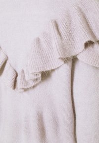 Tissu en tricot rose doux avec un détail froncé le long d'une couture, montrant la texture et les plis du matériau.