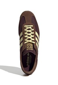 Adidas-sneaker med bruna textil- och mockamaterial, beigefärgade snören, tre beigefärgade ränder och en texturerad gyllene detalj på tungan.