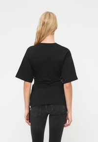 Μαύρο T-shirt με κοντά μανίκια, άνετη εφαρμογή και δέσιμο με κορδόνια στο πλάι, σε συνδυασμό με μαύρο τζιν υφάσμα. Λεπτό ύφασμα με μίνιμαλ σχεδιασμό.