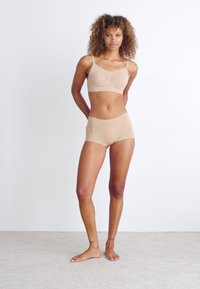 Beige seamless bralette with a ruched front and adjustable straps, paired with matching high-waisted boyshorts. Smooth fabric, minimal design.