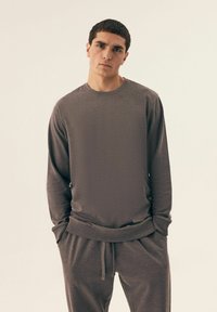 Szara koszulka z długim rękawem, o luźnym kroju, wykonana z miękkiego materiału, z okrągłym dekoltem i ściągaczami przy rękawach, zestawiona z pasującymi spodniami dresowymi.