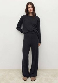 Set di abbigliamento da casa in maglia grigio scuro composto da un top a maniche lunghe e pantaloni a gamba larga, abbinato a calzature simili a pantofole beige. Texture morbida.