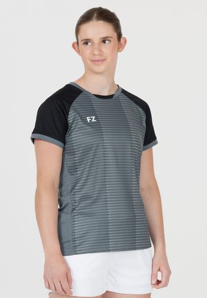 Ung person iført en grå og sort sportstrøje med prikmønster og hvide shorts, der kigger lidt til siden.