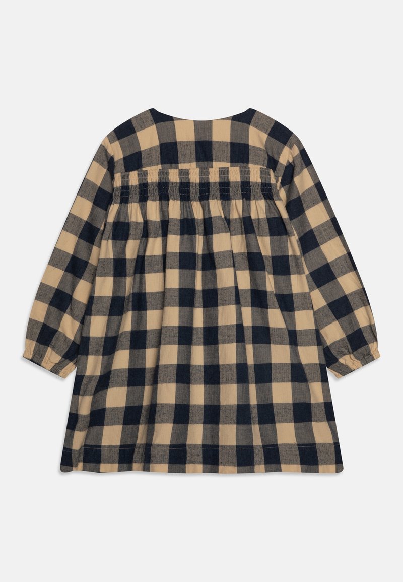 Robe à manches longues beige et noire à carreaux, avec un détail froncé à smocks sur le dos et des poignets élastiqués.