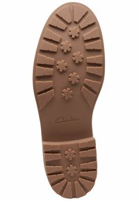 Semelle de chaussure en caoutchouc brun avec des crampons profonds et des motifs en forme d'étoile, portant le nom de la marque "Clarks" embossé près du talon.