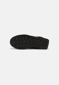 Semelle de chaussure en caoutchouc noir avec un motif de bande de roulement triangulaire profond pour l'adhérence, présentée horizontalement sur un fond blanc uni.