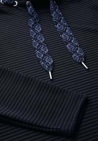 Felpa con cappuccio a coste scure e lacci blu a motivo in contrasto. Presenta occhielli in metallo argentato e un tessuto testurizzato.