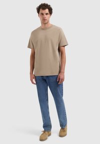 Beige katoenen T-shirt met een ronde halslijn en korte mouwen, gecombineerd met blauwe spijkerbroeken en beige schoeisel.