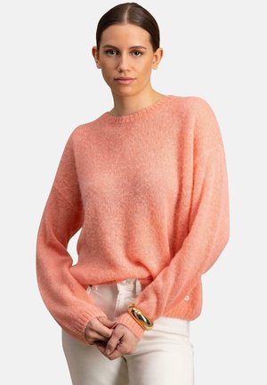 Jasnoróżowy sweter wykonany na drutach z okrągłym dekoltem, w oversize'owym fasonie i z ribbowanymi mankietami. Miękka tekstura i mały guzik zdobniczy przy dolnym brzegu.