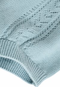 Pull en maille bleu clair avec des motifs texturés, des poignets côtelés et une finition douce, mettant en valeur des coutures détaillées le long du tissu.