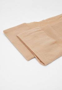 Beige knelange sokker laget av myk, teksturert stoff, med ribbet design på toppen og en jevn overflate på kroppen.