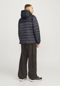 Black puffer jacket with a hood, featuring a quilted texture, elastic cuffs, and a relaxed fit, paired with loose, dark trousers and black sneakers.