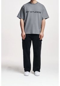 Szary bawełniany t-shirt z krótkim rękawem, z napisem "2Y STUDIOS" w kolorze czarnym. Do tego czarne spodnie typu cargo i białe sneakersy.