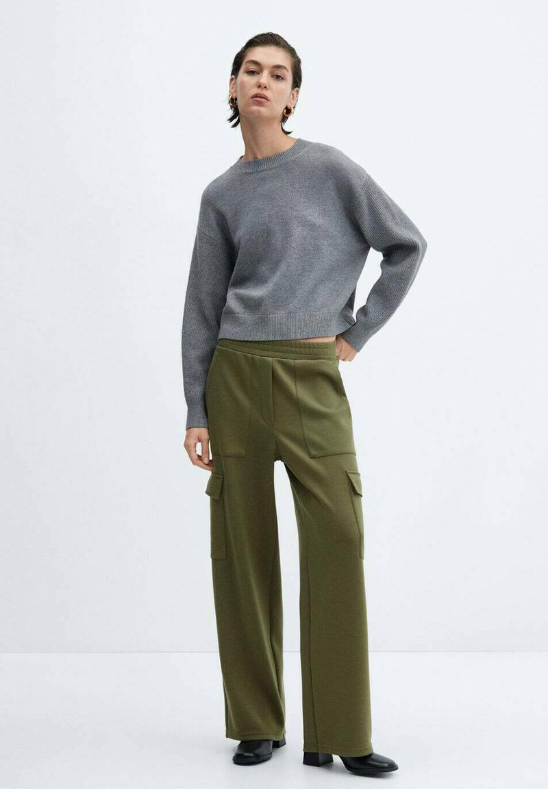 Suéter gris corto con puños acanalados combinado con pantalones cargo verdes olivo de pierna ancha que cuentan con dos bolsillos laterales. Botines negros de tobillo completan el look.