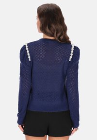 Marineblauer Strickpullover mit strukturierter, offener Webart, ausgestattet mit Puffärmeln und verzierten Schulterakzenten in einer hellen Farbe.