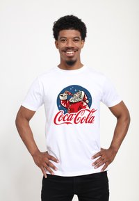 Hvid bomulds t-shirt med et retro Santa Claus grafisk design, livlige røde og blå farver, samt "Coca-Cola" tekst i kursiv stil.