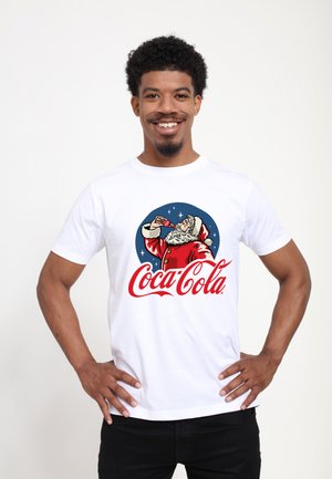 White cotton t-shirt featuring a retro Santa Claus graphic, vibrant red and blue colors, and "Coca-Cola" text in cursive style.