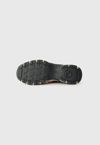 Black rubber outsole with textured grip pattern and beige accents. Sturdy construction with a circular emblem near the heel area.