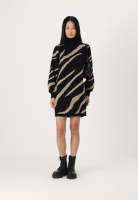 Schwarzes Langarmkleid mit einem beigen Tigerstreifenmuster. Das Kleid hat einen Stehkragen und wird mit schwarzen Schnürkampfschuhen kombiniert.