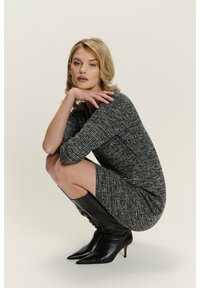 Stylizované černé pletené šaty se třetinovými rukávy, zdobené modrými a žlutými akcenty, v kombinaci s černými koženými vysokými botami s špičkou.