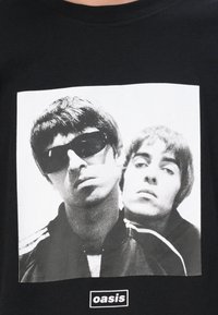 Black cotton t-shirt featuring a white graphic print of two figures in sunglasses, with "oasis" label at the bottom.