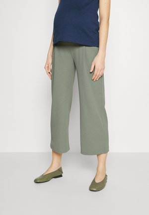 Pantalones verdes de pierna ancha en una tela suave y ligera, combinados con una blusa ajustada azul oscuro y zapatos planos verdes con un pequeño tacón.