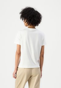 Hvid bomulds-T-shirt med en afslappet pasform, korte ærmer og rund hals, samlet med lysebeige bukser. Minimalistisk design.