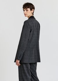 Blazer grigio a quadri con colletto in pelle nera. Design monopetto, vestibilità su misura e dettagli in bottone sulle maniche.