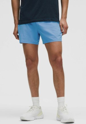 Light blue athletic shorts with a smooth texture, mid-thigh length, and elastic waistband, paired with white sneakers and light socks.